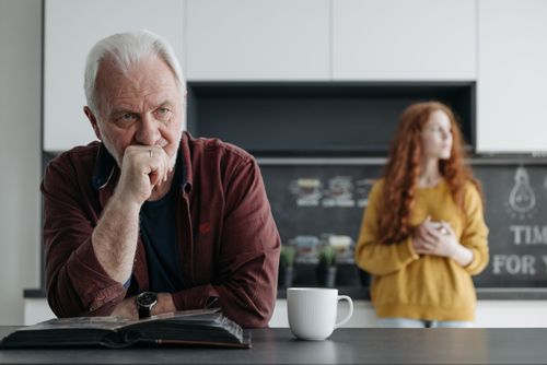 Free Elderly man looking thoughtful in a kitchen, with a young woman in the background, conveying a scene of contemplation and emotion. Stock Photo