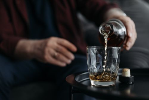 Free An adult pours whiskey from a bottle into a glass on a table. Indoors setting. Stock Photo