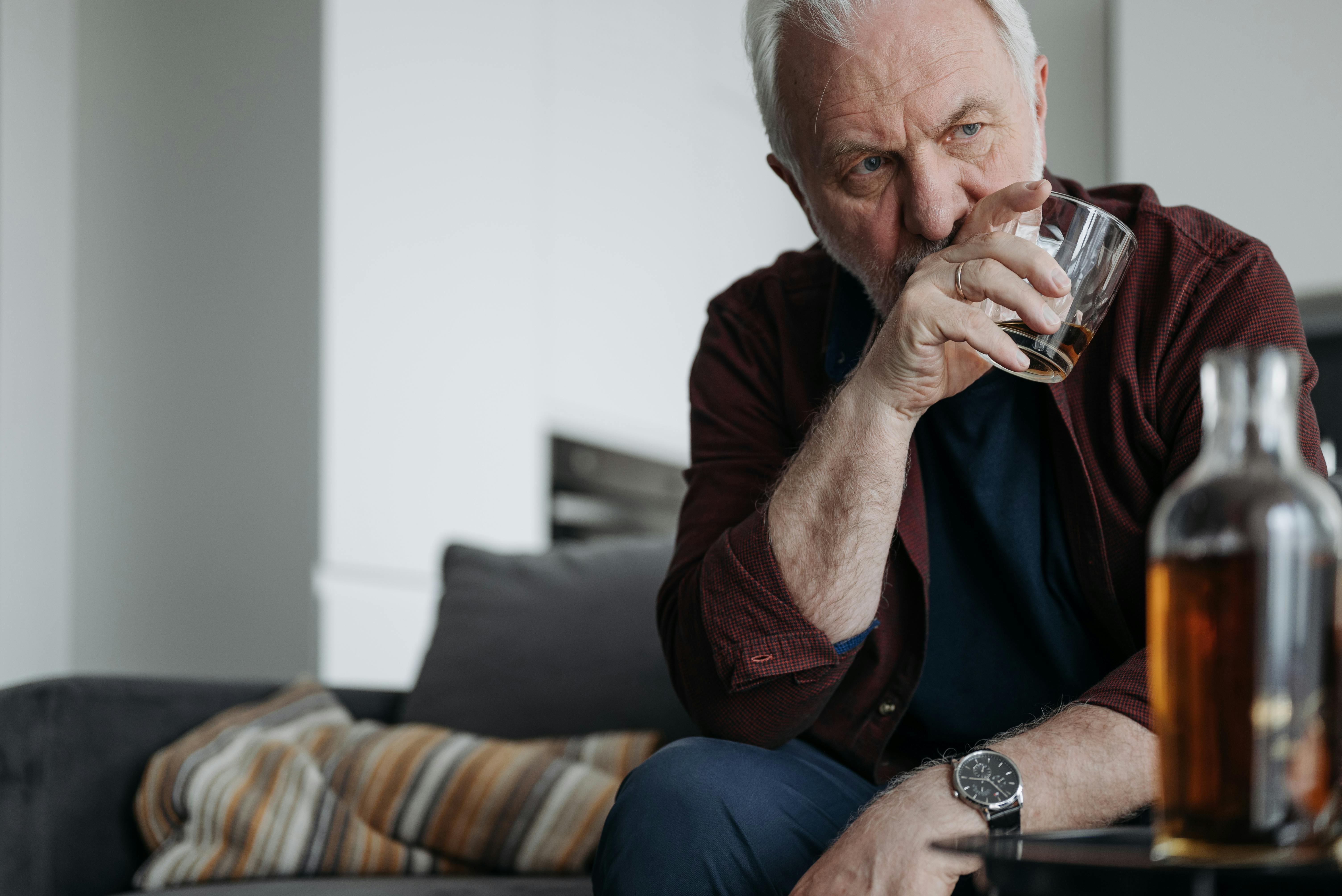 Pensive senior man sitting indoors with a drink, reflecting on his thoughts.