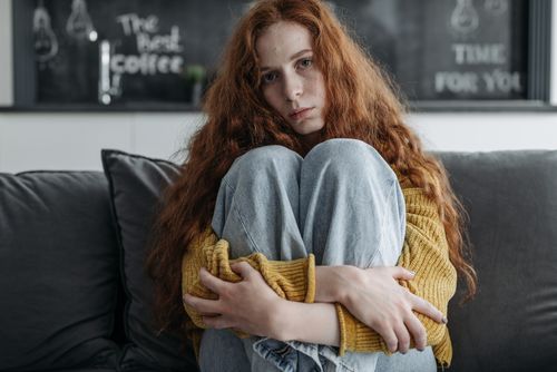 Free Young woman with red hair sitting indoors, expressing introspective emotion. Stock Photo