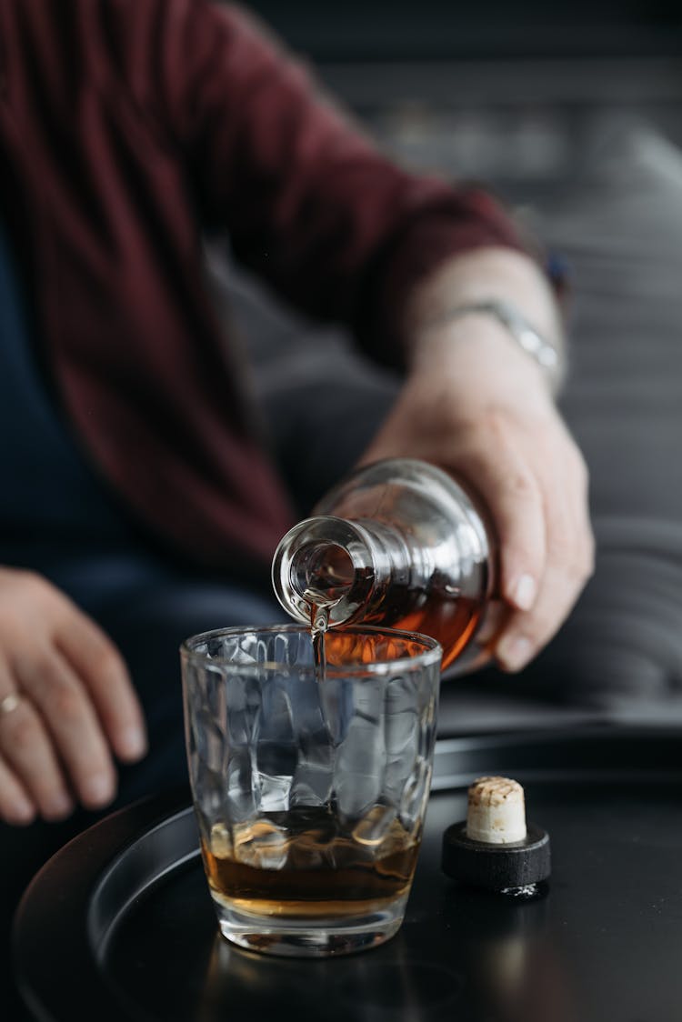 Person Pouring Liquor On A Glass Cup