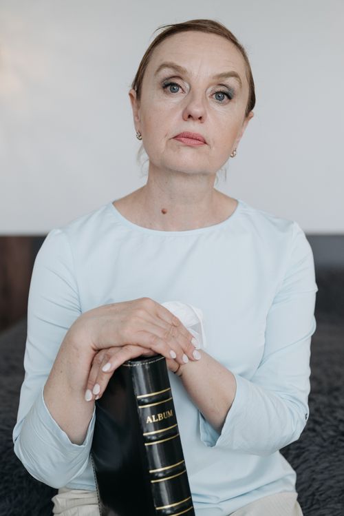 Free A mature woman with a serious expression holding a leather-bound photo album indoors. Stock Photo