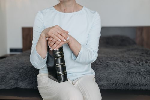 Free Adult woman sitting on bed with a closed photo album in her hands, indoors. Stock Photo