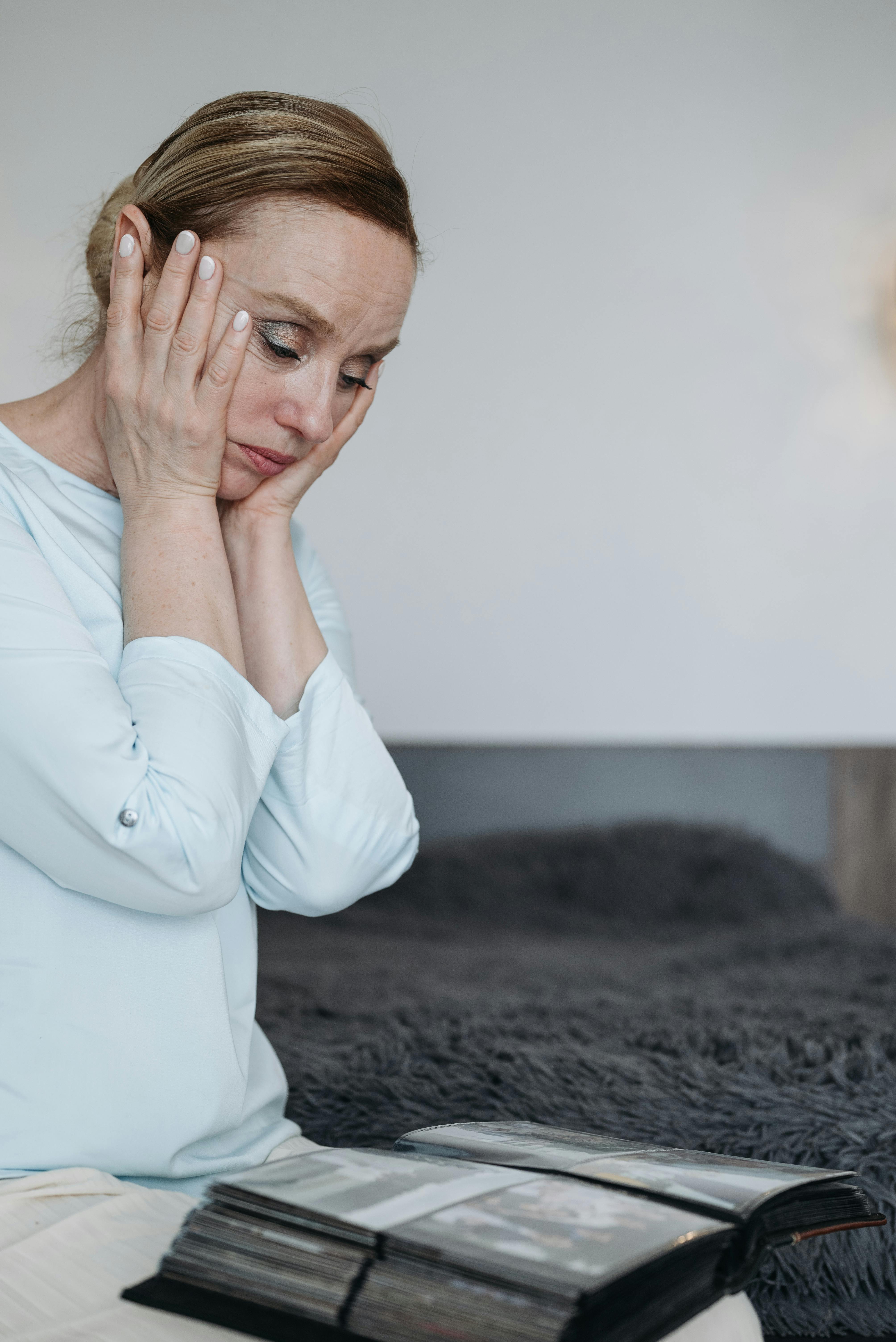 A pensive woman sits in her bedroom looking at a photo album, evoking emotions and memories.