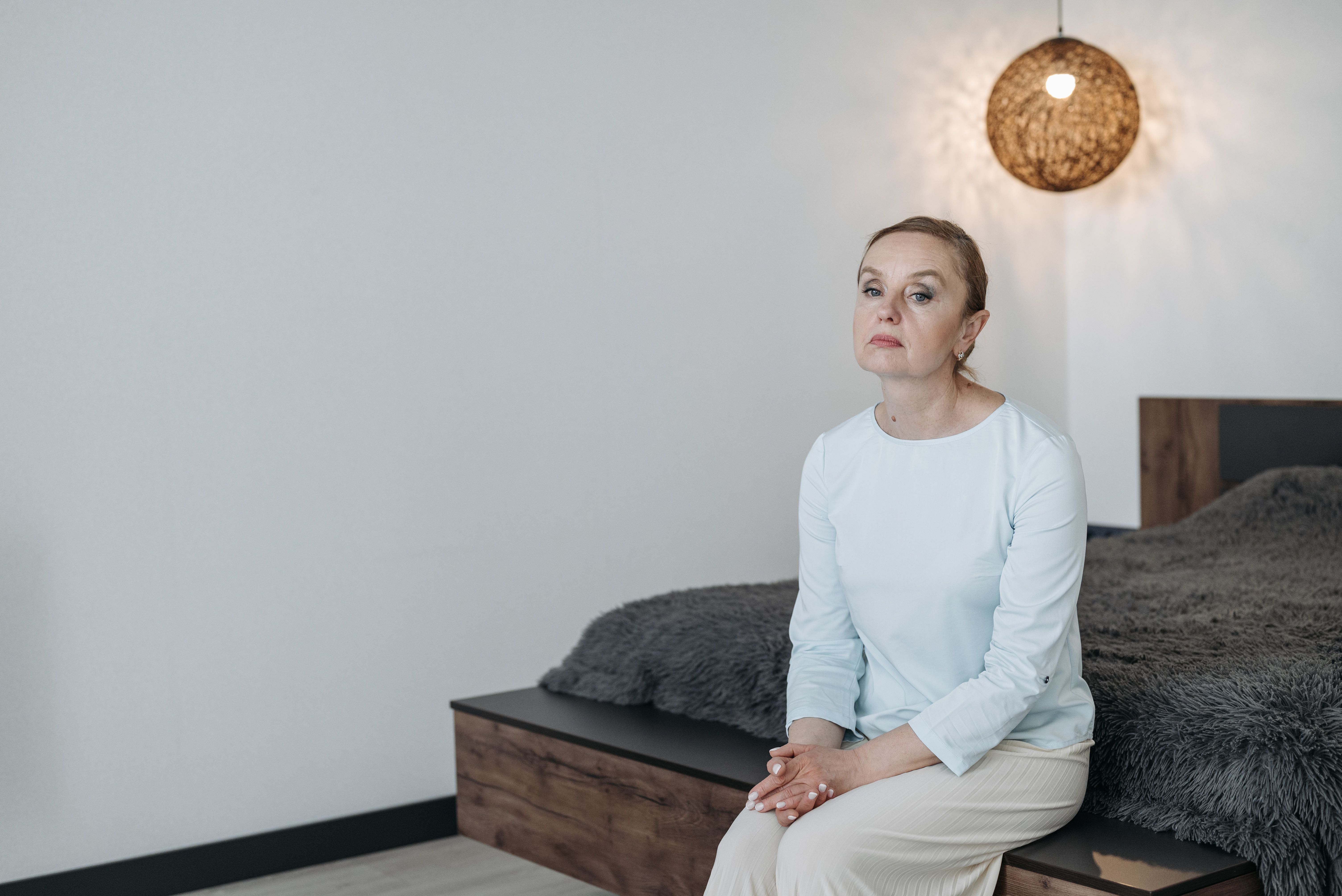 A middle-aged woman sitting on the edge of her bed at dawn after a night of disrupted sleep