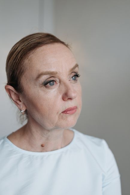 A midlife woman in a kitchen, calm, holding a mug, mid-thought.