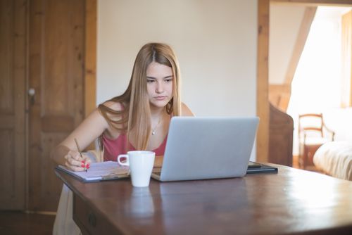 Free Focused young woman working at home with a laptop, writing notes. Ideal setting for remote work or studying. Stock Photo