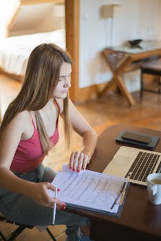 A woman working from home with a laptop and documents in a cozy room setting.