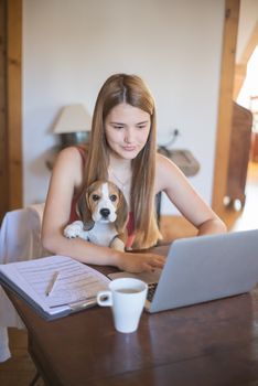 A young woman using a laptop at home with her beagle on her lap.