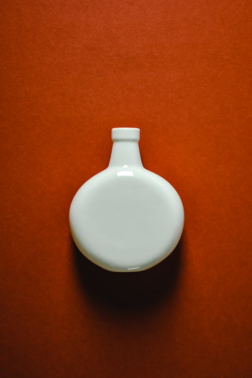 A White Ceramic Vase on Orange Surface