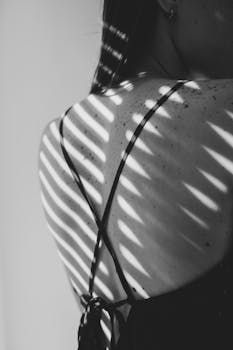 Monochrome image showcasing dynamic shadows on a woman's back with freckles.