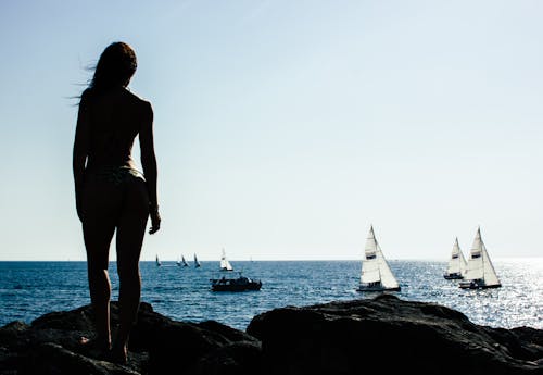 Free Woman Standing on Rock With Sailing Boats on Sea Stock Photo