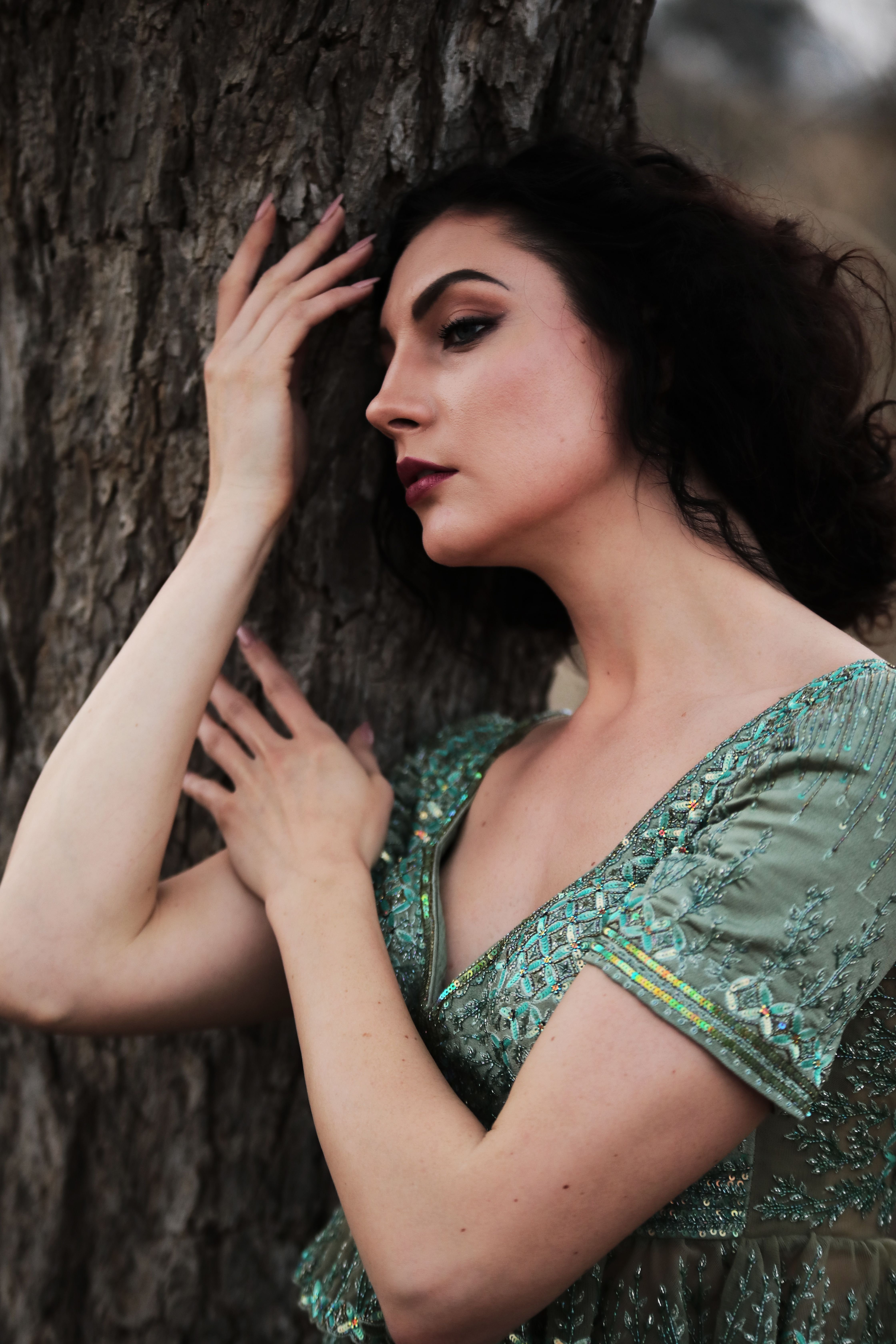 A woman in a green dress leaning against a tree, exuding elegance and grace.