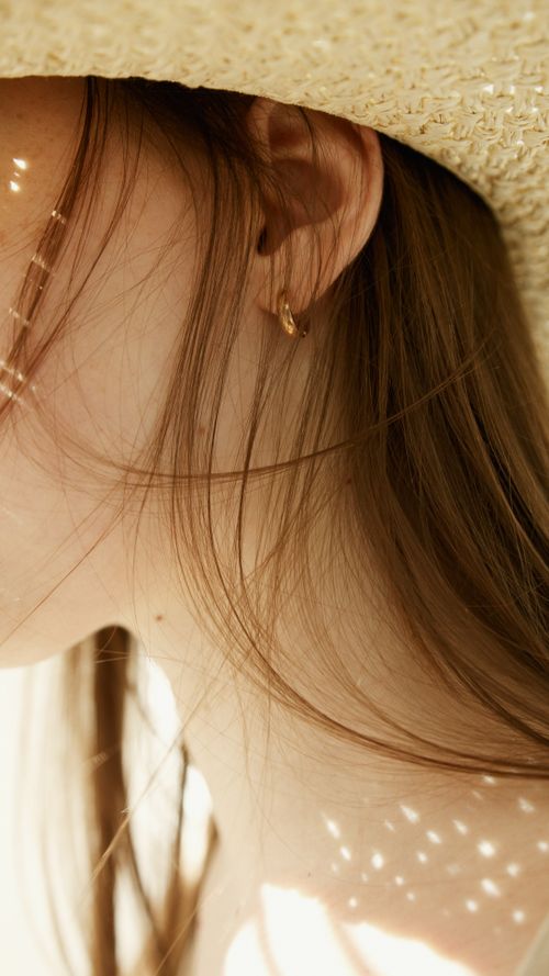 Free Artistic close-up of a woman's ear adorned with an earring, under a straw hat. Stock Photo