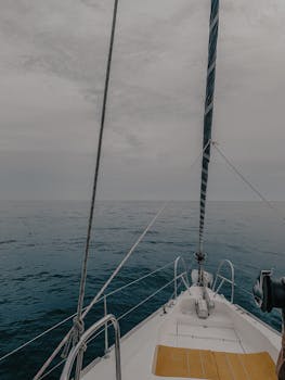 View from a sailboat deck amidst calm ocean waters, under a cloudy sky.