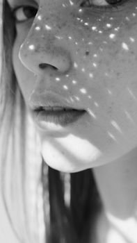 Close-up black and white portrait of a woman with freckles illuminated by patterned sunlight