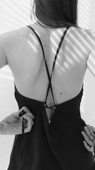 Grayscale image of a woman adjusting the back of her dress with detailed light and shadow play.