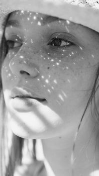 Close-up black and white portrait of a woman with freckles, adorned with shadows.