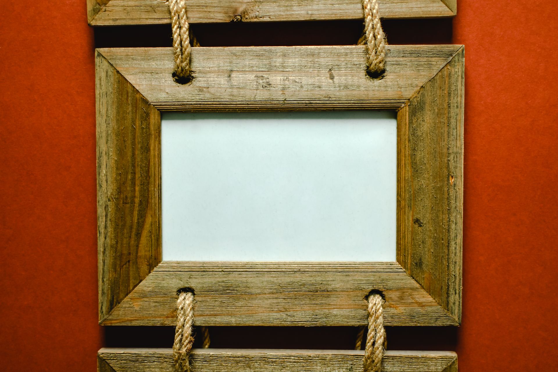 A rustic wooden photo frame with rope detail against a red background, perfect for decor themes.