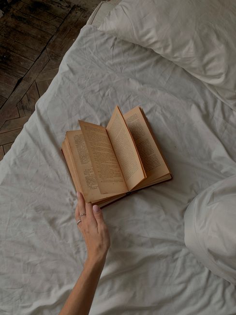 A hand flipping through an open book on a bed, creating a cozy and relaxing atmosphere.