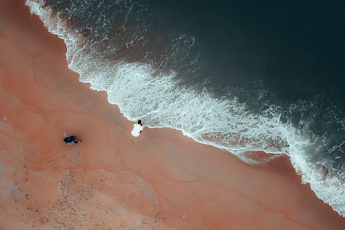 Anonymous travelers admiring powerful ocean from sandy coast