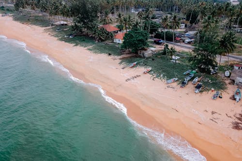 Sandy beach washing by wavy sea on sunny day in tropical village