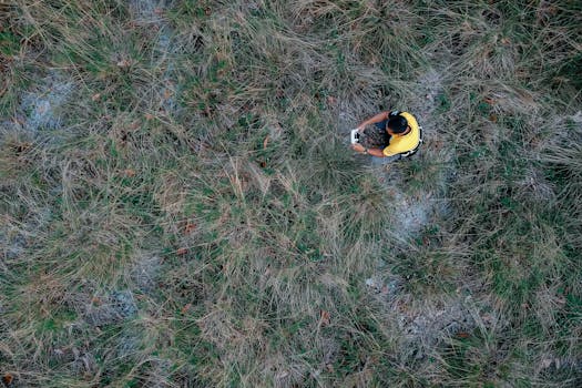 Top-down view of a man with a drone controller in a grassy meadow in Terengganu.