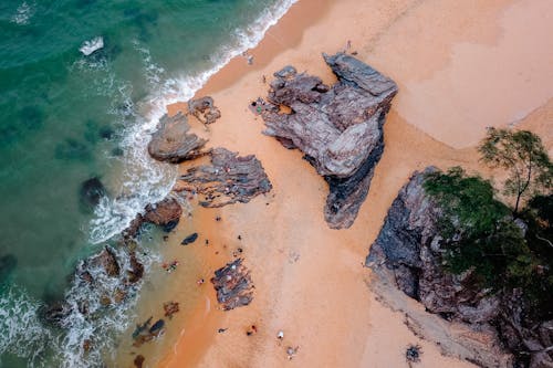 Free Breathtaking aerial view of rough rocky formations on wet sandy beach washing by picturesque turquoise wavy ocean on sunny day Stock Photo