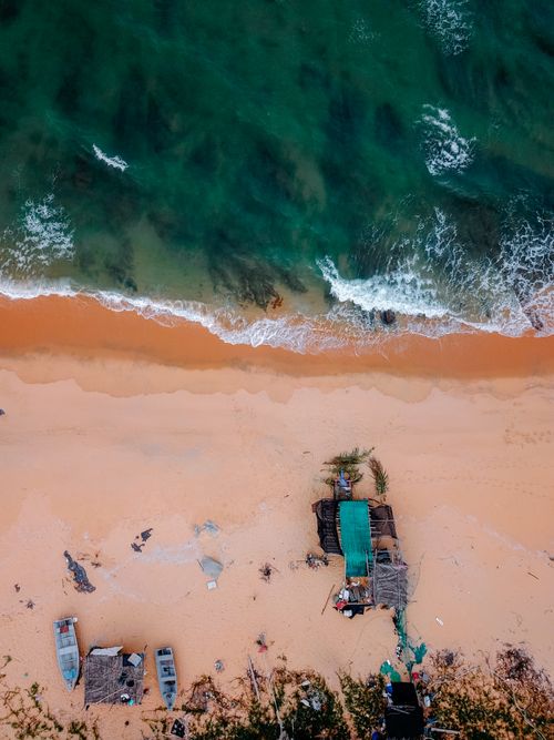 Free Breathtaking aerial view of powerful turquoise sea with foamy waves splashing on sandy beach with moored old wooden boats in daytime Stock Photo