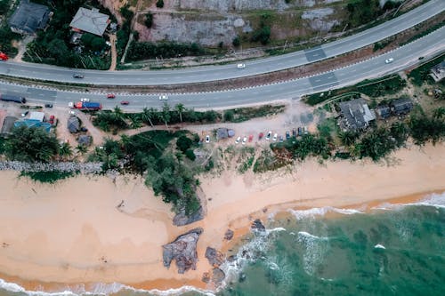 Breathtaking drone view of cars driving on asphalt road near picturesque sandy beach washing by turquoise ocean on sunny day