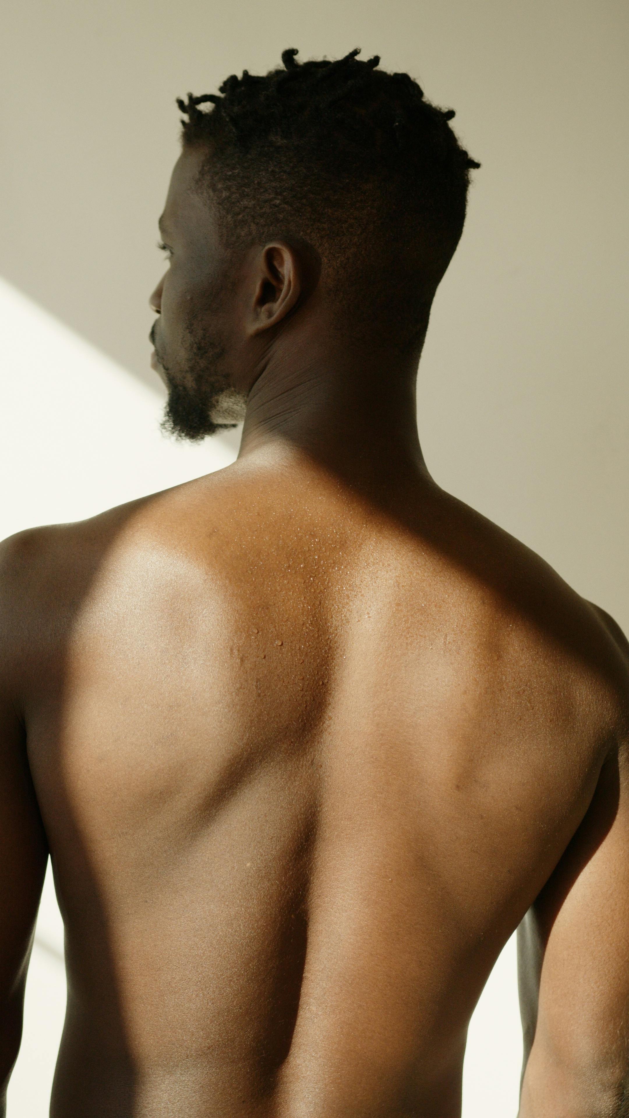 A shirtless African American man viewed from behind, highlighting natural lighting on skin.