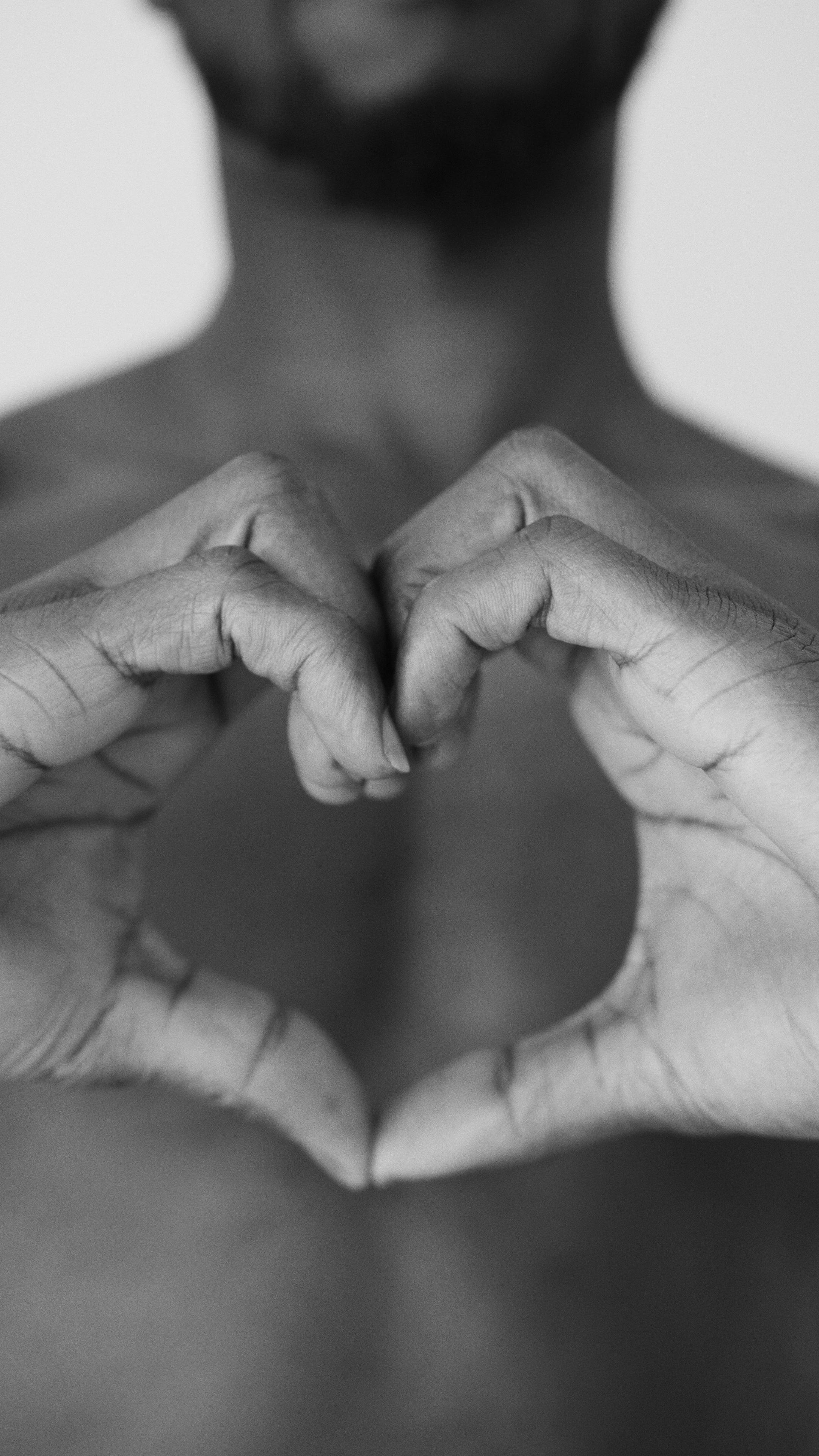 Close-up of hands forming a heart shape in a black and white image, symbolizing love.