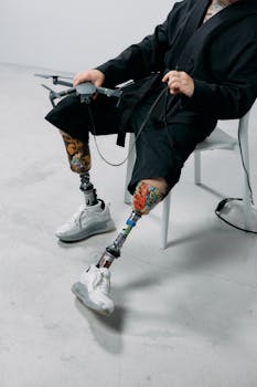 Person with prosthetic legs sitting indoors using a drone controller, demonstrating technology integration.