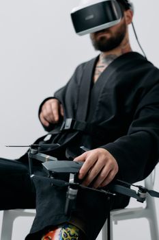 A man sitting indoors using a VR headset and holding a drone, suggesting modern technology interaction.