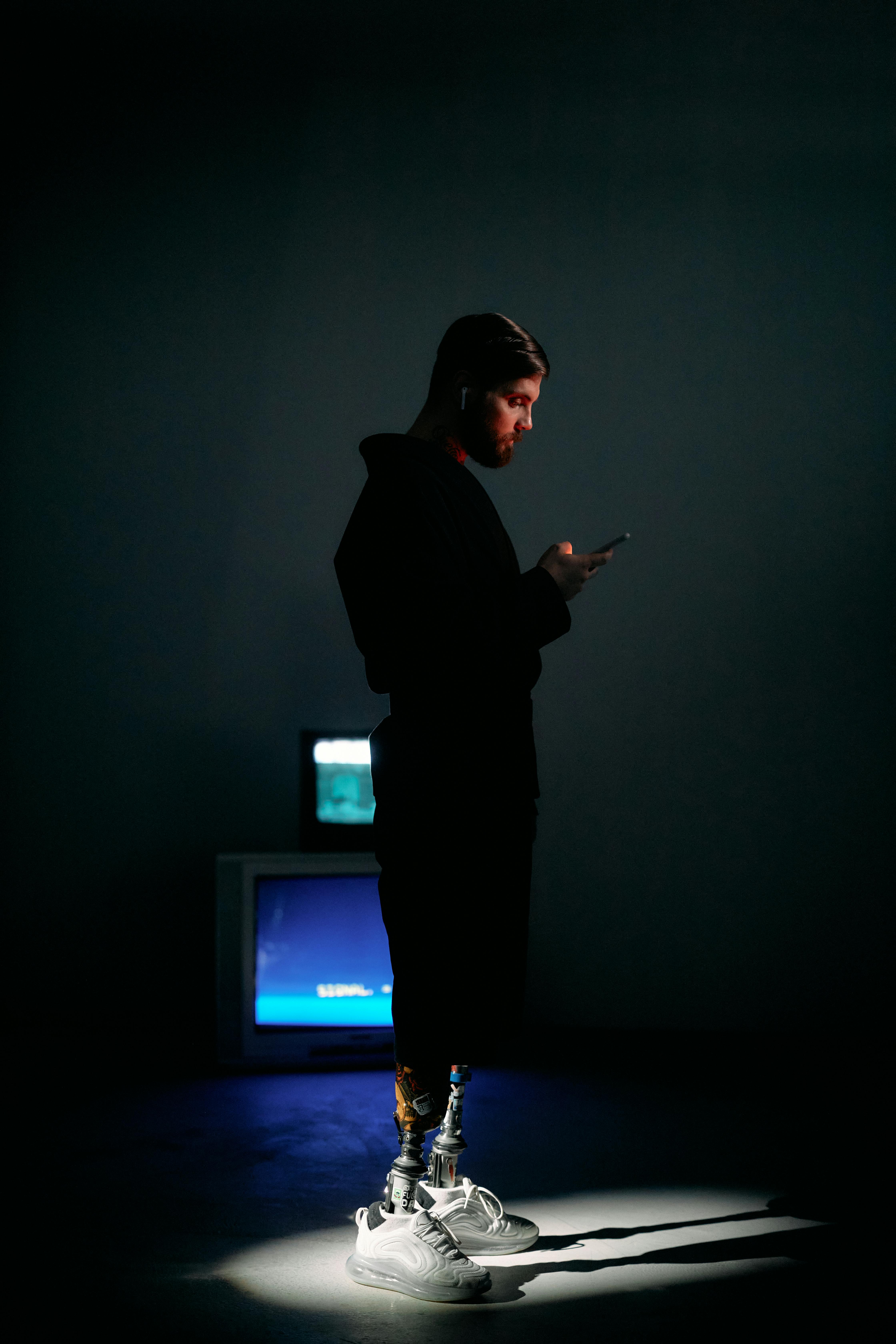 Side view of a man with prosthetic legs browsing a smartphone in a dimly lit room.