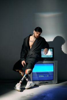 Bearded man in studio sitting on vintage CRT TV, showcasing technology integration and modern style.