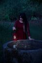 Woman in Red Dress Holding an Oil Lamp While Looking at a Deep Well