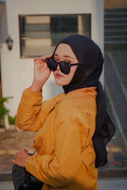 Free Photo of a Woman in a Black Hijab Looking at the Camera while Touching Her Sunglasses Stock Photo