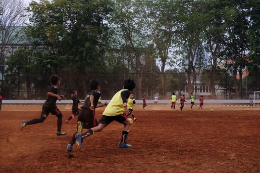 Group of kids playing soccer on a dirt field with trees in background, showcasing teamwork and sportsmanship.