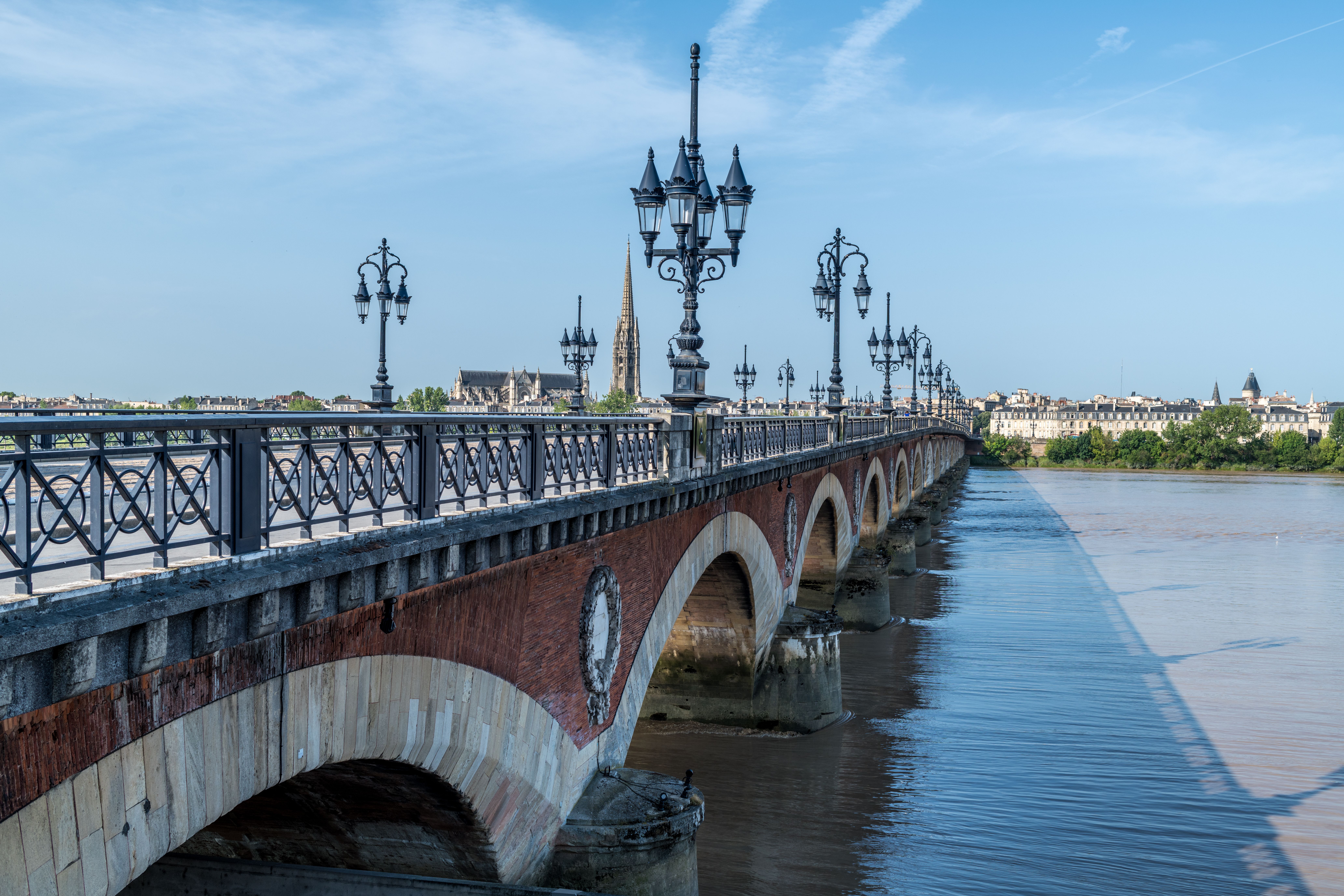 Fotomural Vista escénica del icónico puente Pont de Pierre en Burdeos bajo un cielo azul, reflejándose en las aguas tranquilas del río Garona.