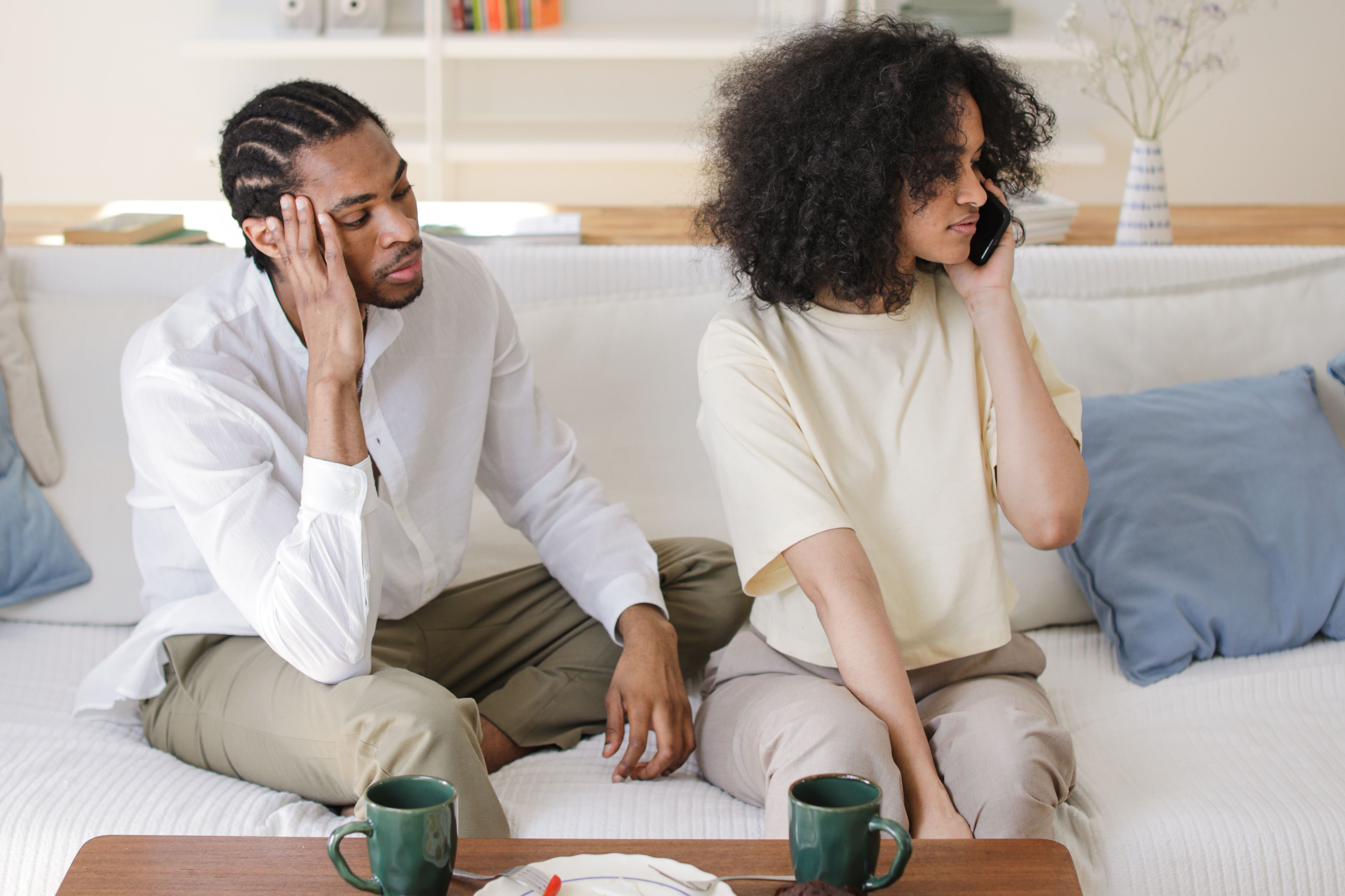 A couple sitting on a couch, one person using a smartphone, depicting modern relationship dynamics.