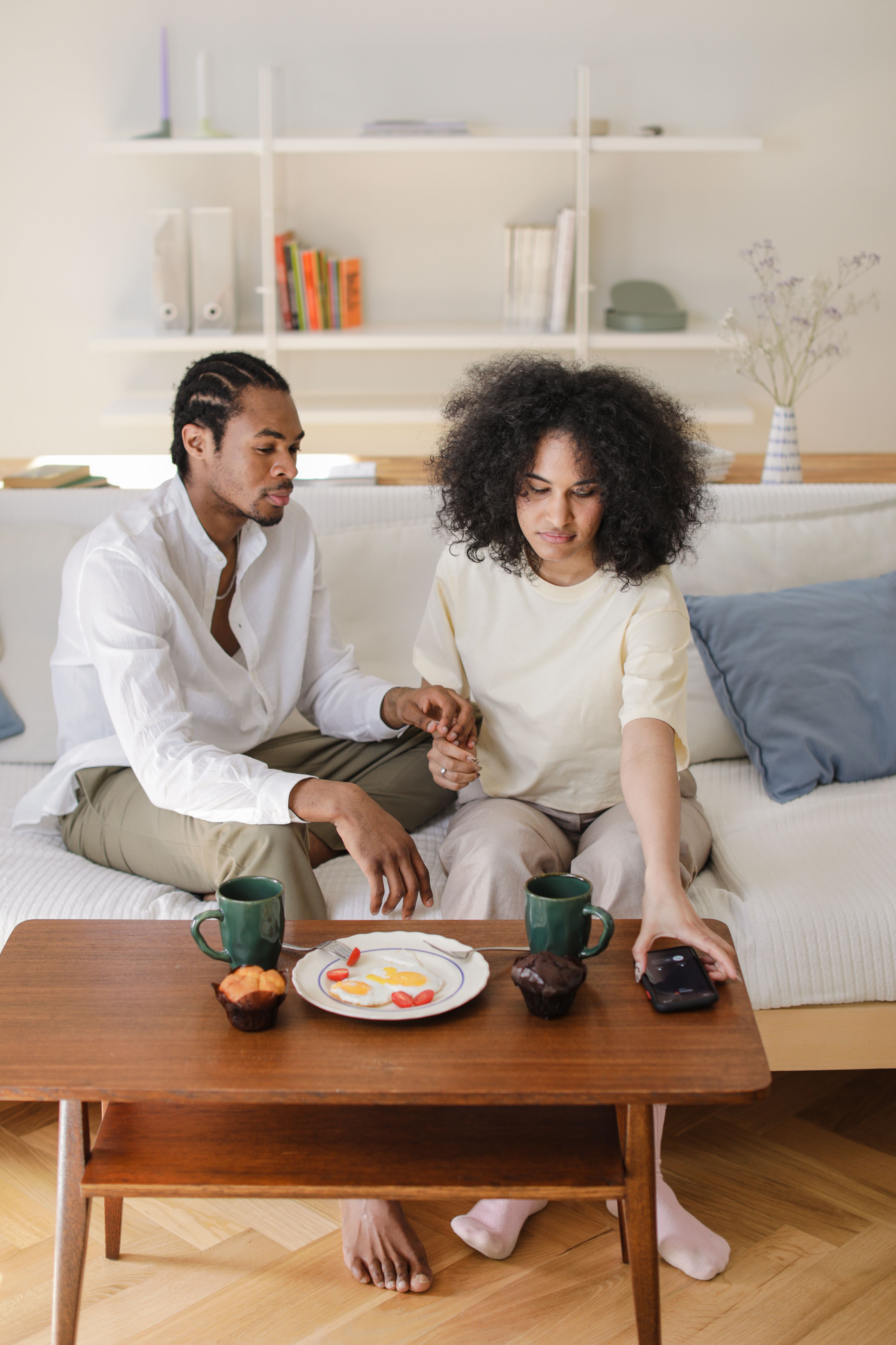 A couple sitting on a sofa, enjoying a relaxing moment with snacks and coffee at home.
