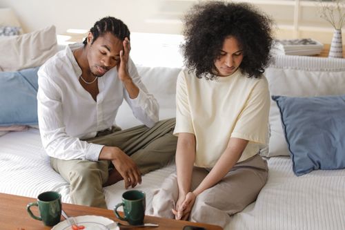 Free A contemplative black couple sitting on a sofa indoors in a modern setting, reflecting emotions. Stock Photo