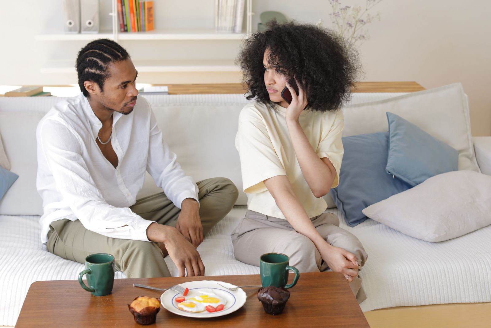 Two people seated on a sofa with mugs while one holds a phone