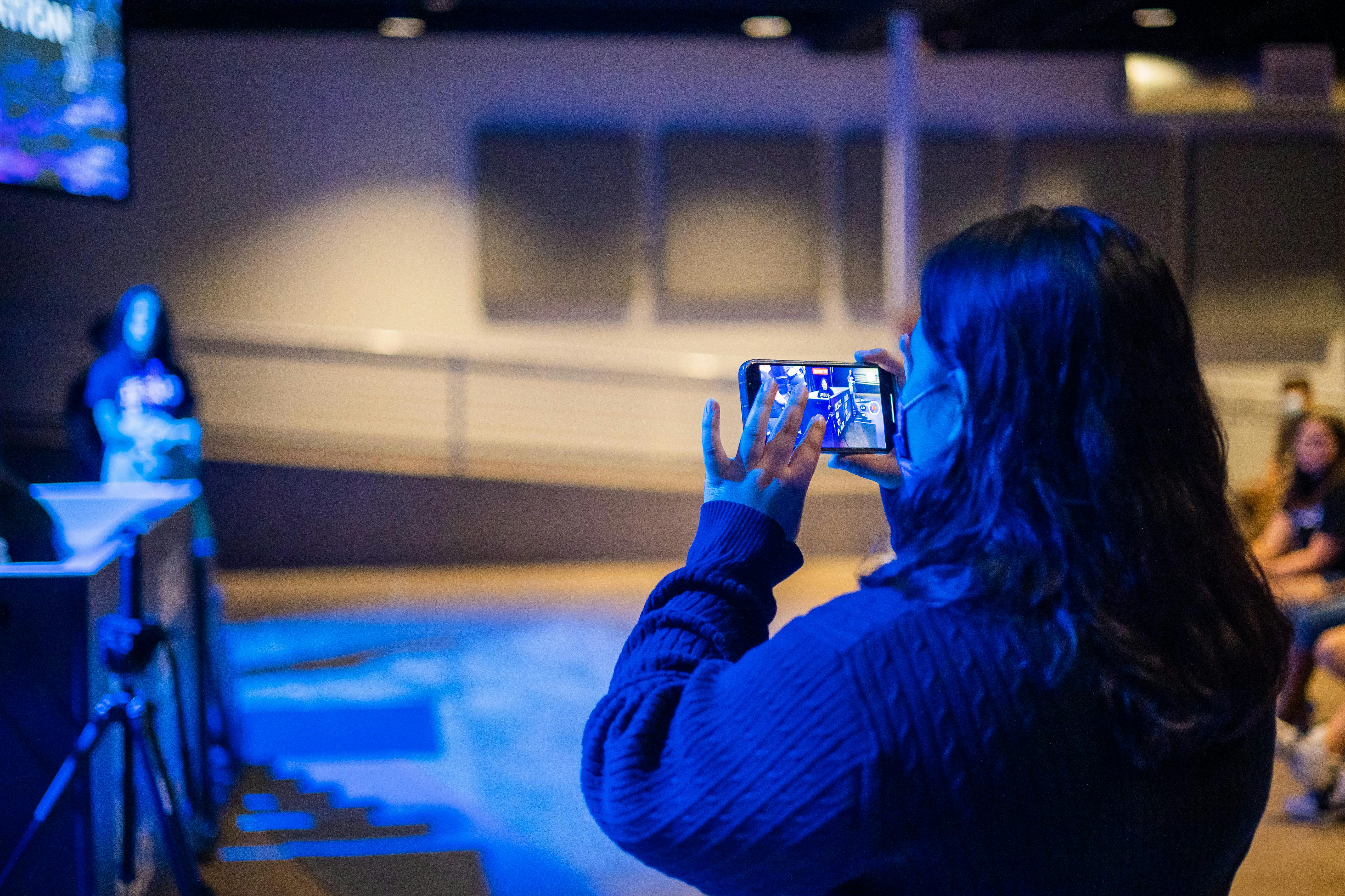 Free A woman capturing a moment indoors using her smartphone at an event. Stock Photo
