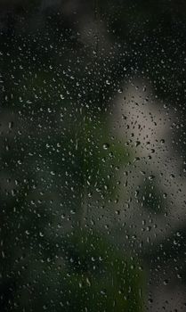 Close-up of a window with rain droplets creating a serene outdoors view in Odisha, India.