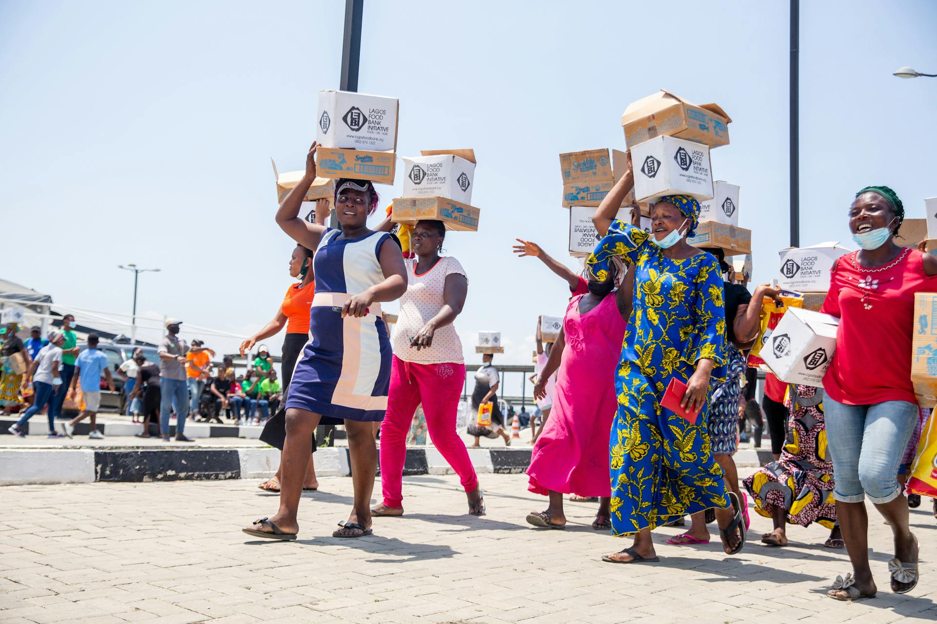 A vibrant scene of women carrying donation boxes on a sunny street, symbolizing community spirit.