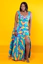 Full body of African American female wearing trendy colorful ornamental maxi dress and high heels looking down on yellow background in studio
