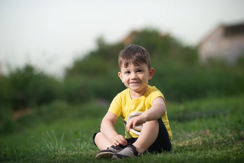 Free Cute young boy in yellow sitting on green grass, enjoying a sunny day outdoors. Stock Photo