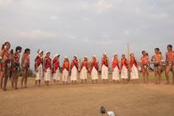 A group of adults in traditional tribal attire performs a dance ceremony outdoors.